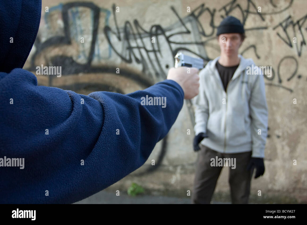 Uomo in giacca con cappuccio pistola di puntamento al rivale Foto Stock