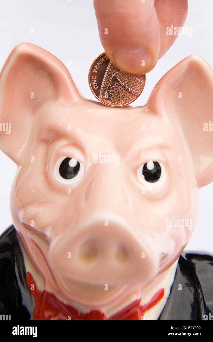 Un uomo mette un centesimo in un salvadanaio. Questo è uno di una serie di cinque banche piggy prodotta dalla NatWest Bank negli anni ottanta. Foto Stock