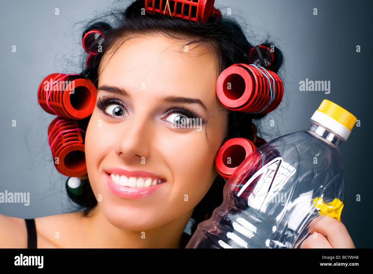Giovani casalinga con i capelli rulli e una bottiglia Foto Stock