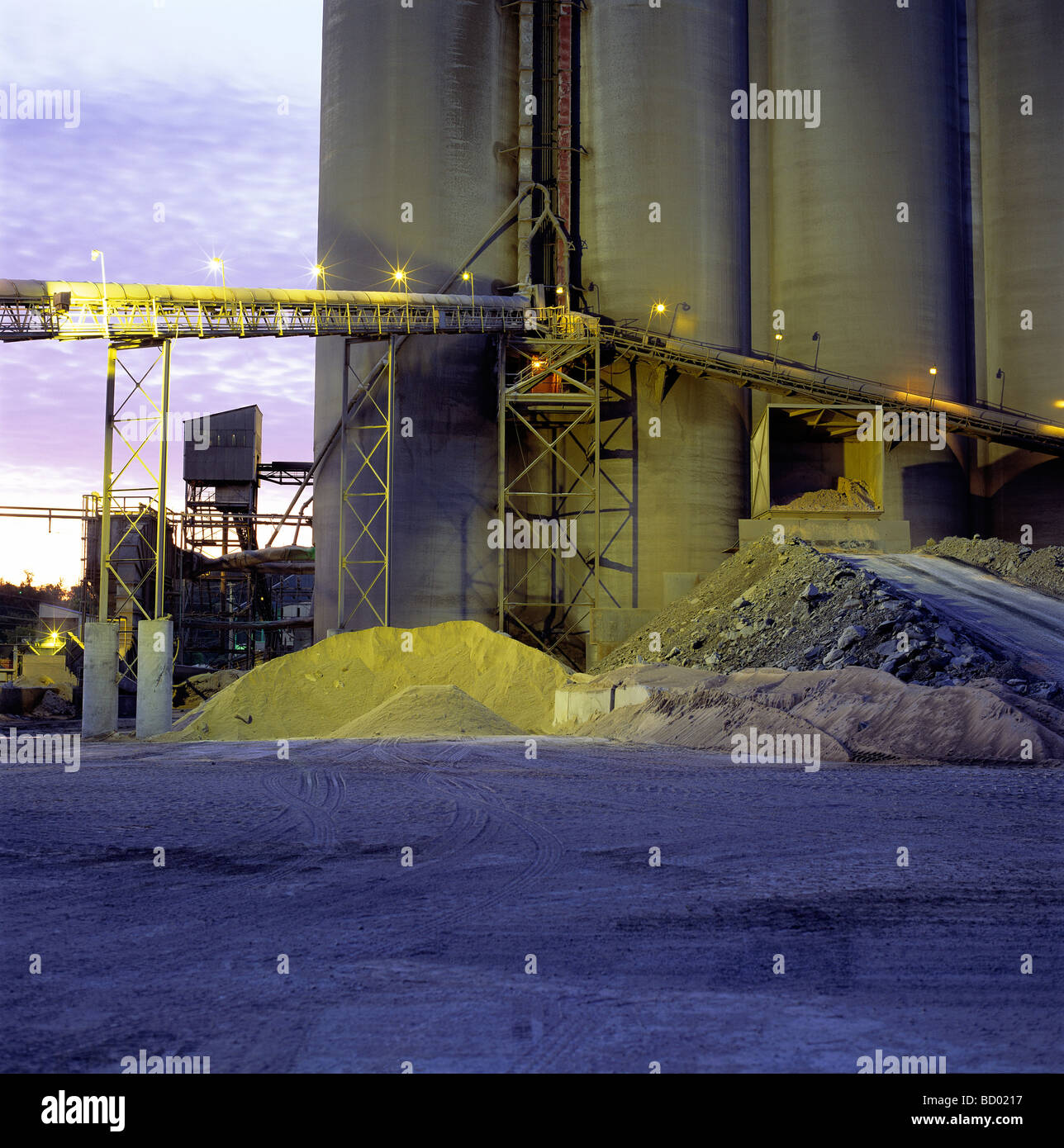 Vista del tramonto di materie prime a nastro trasportatore e silos a un impianto per cemento Foto Stock