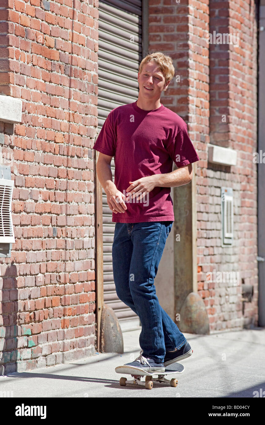 Young Teen rides uno skateboard in giù lungo la strada Foto Stock