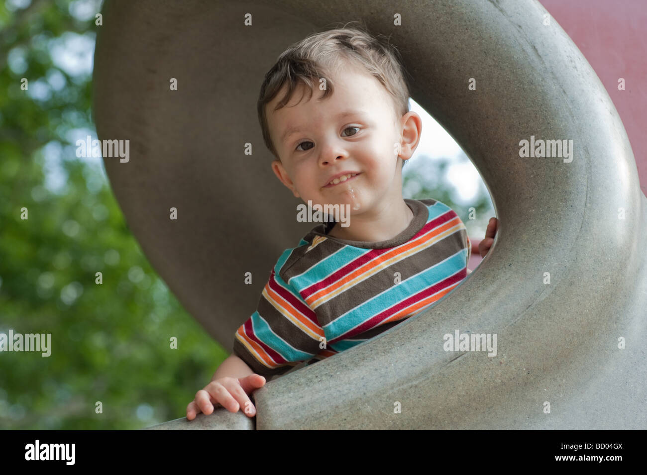 Little Boy giocando su una slitta a parco giochi guardando la fotocamera con un dolce sguardo sul suo viso Foto Stock