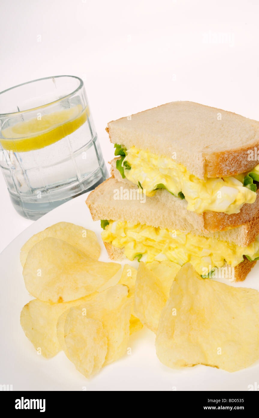 Insalata di uova in sandwich di pane bianco con lattuga patatine e un bicchiere di acqua su sfondo bianco. Foto Stock