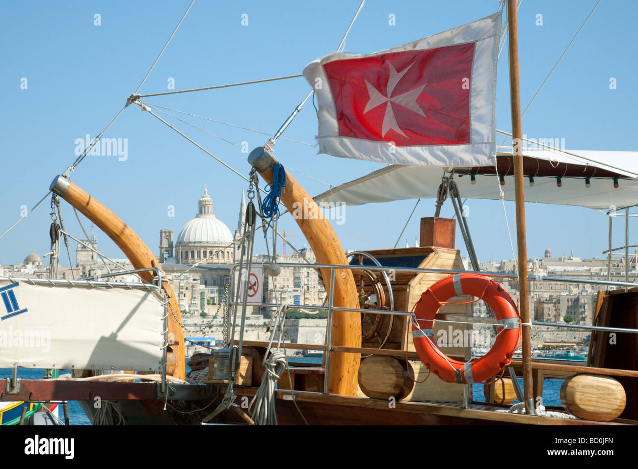 La croce di malta bandiera a bordo di una barca a vela con La Valletta in background, Malta Foto Stock