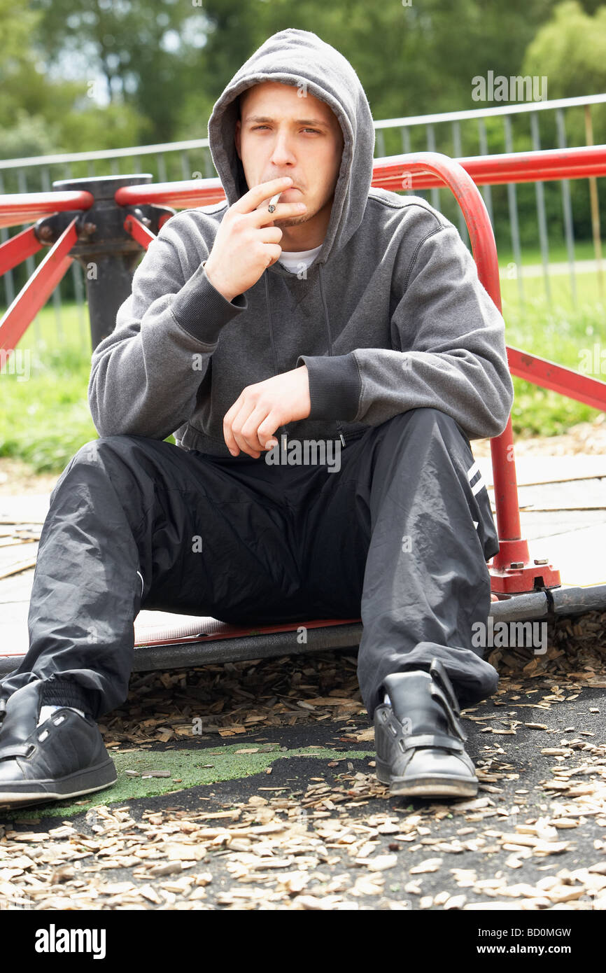 Giovane uomo seduto nel parco giochi giunto per fumatori Foto Stock