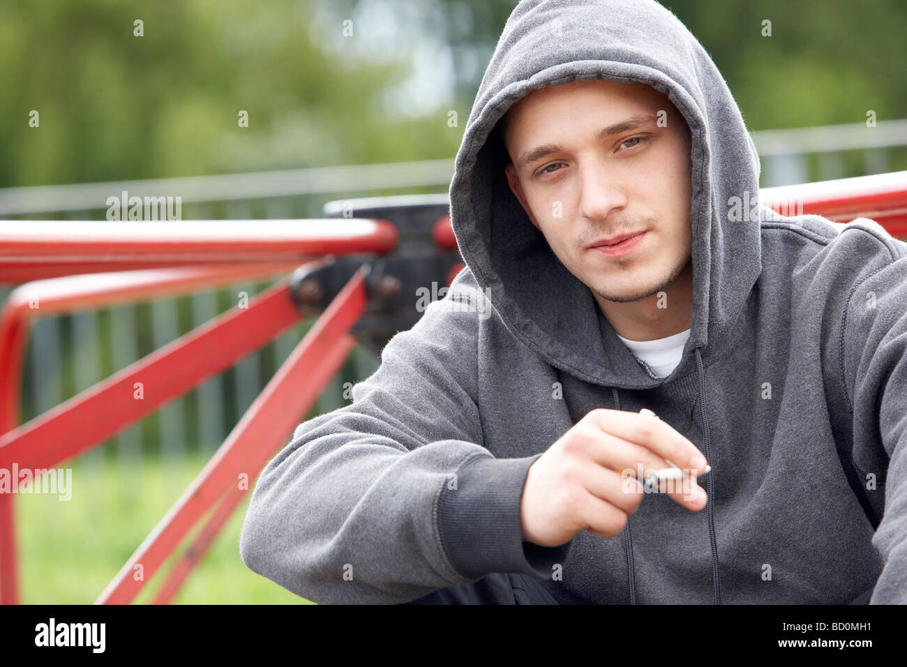 Giovane uomo seduto nel parco giochi giunto per fumatori Foto Stock
