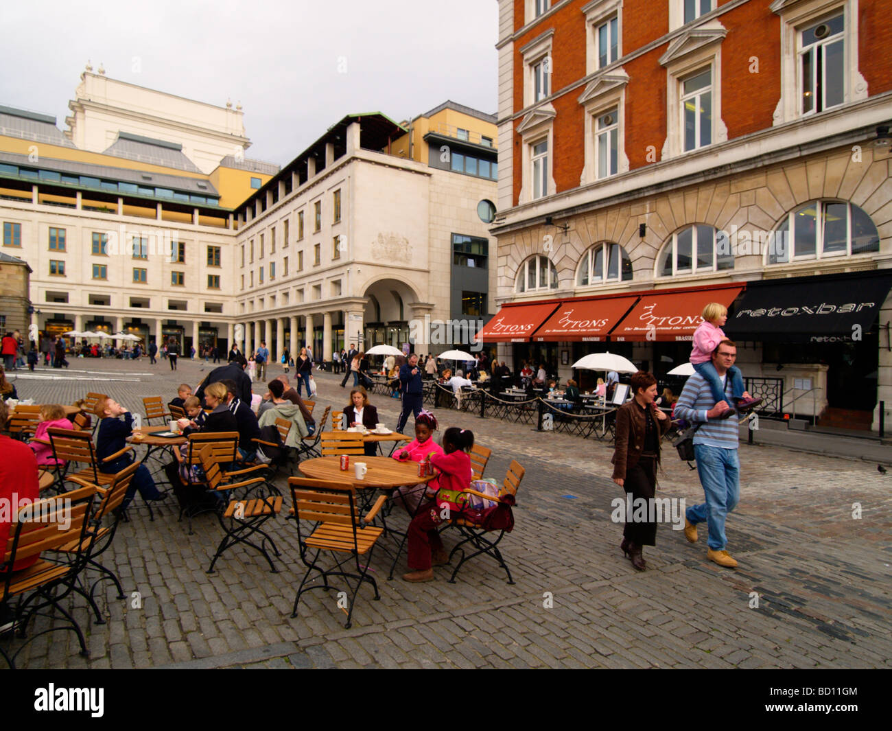Giovane a piedi con i loro bambini e persone sedute presso il cafe' sul marciapiede in Covent Garden London REGNO UNITO Foto Stock