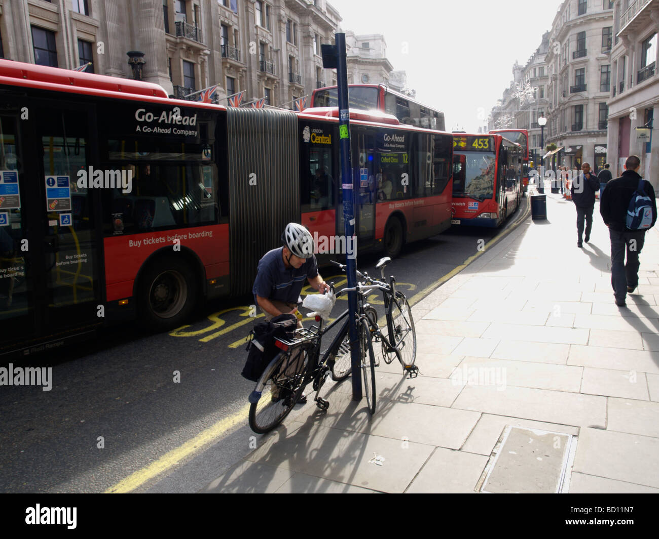 Ciclista disimballaggio la sua bici a Londra s Regent Street con autobus in background London REGNO UNITO Foto Stock