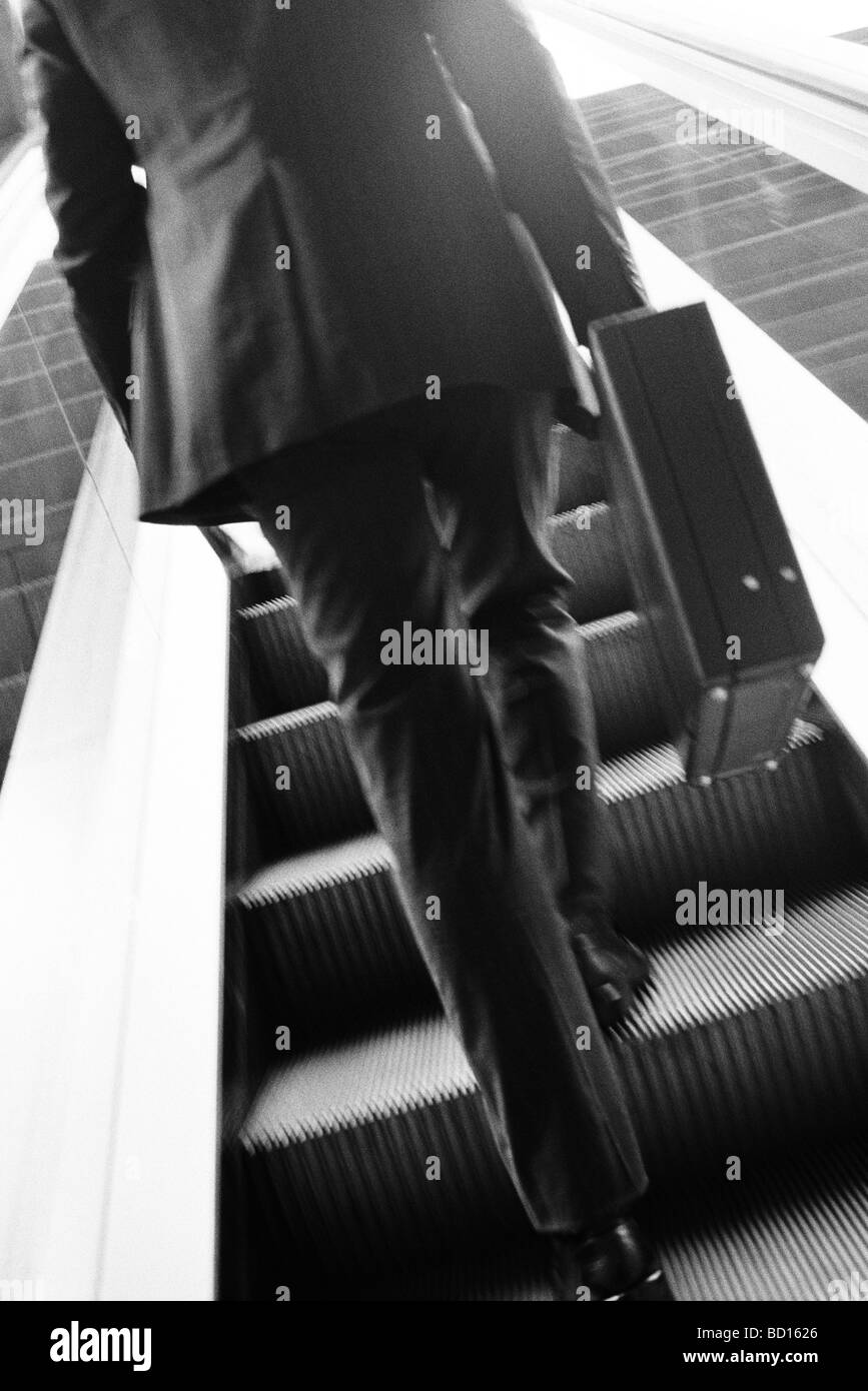 Imprenditore valigetta porta escalator ascendente, vista posteriore Foto Stock