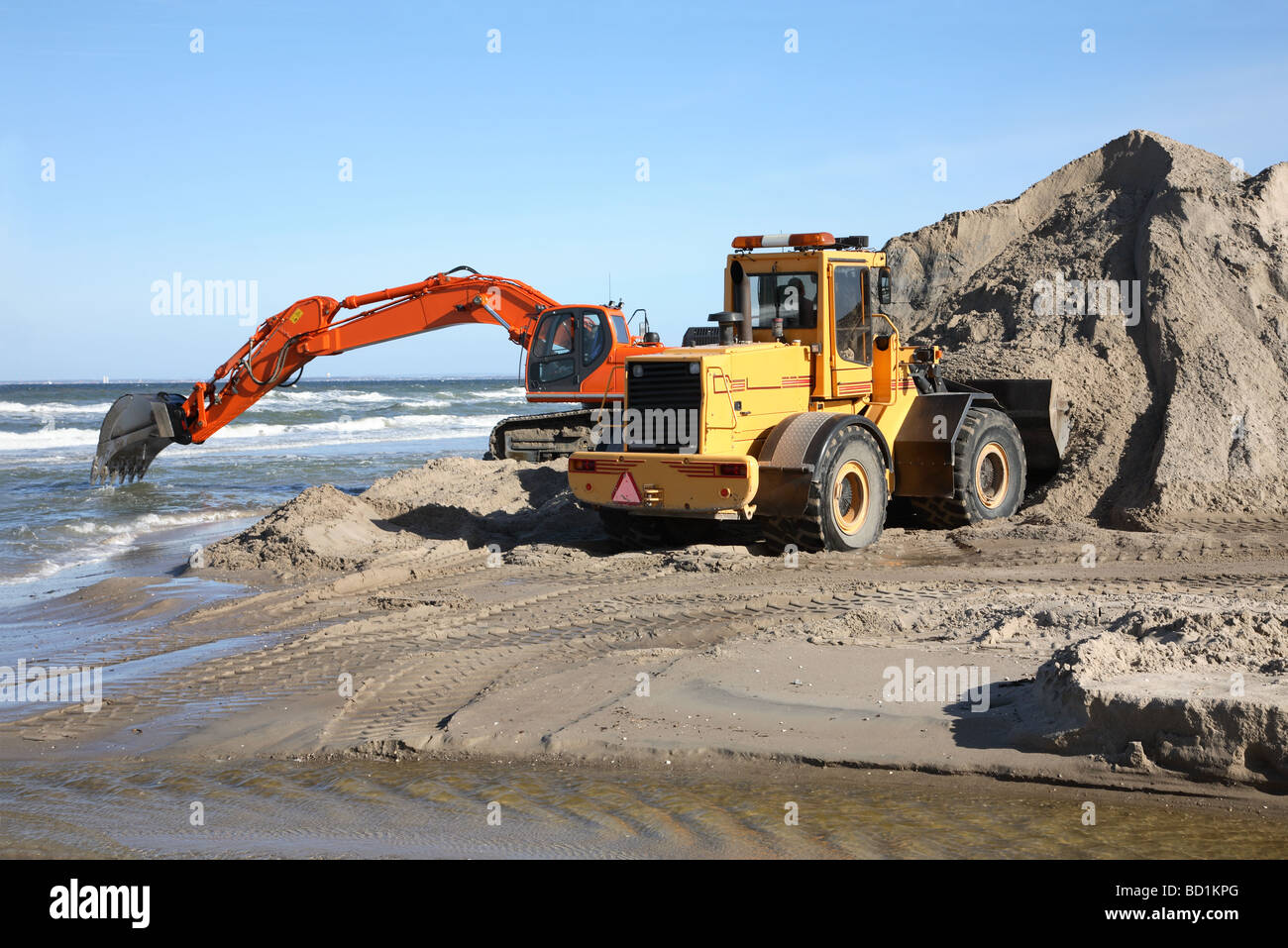 Navvy e caricatore frontale lo scavo e la movimentazione di sabbia in costa un progetto di protezione. Foto Stock