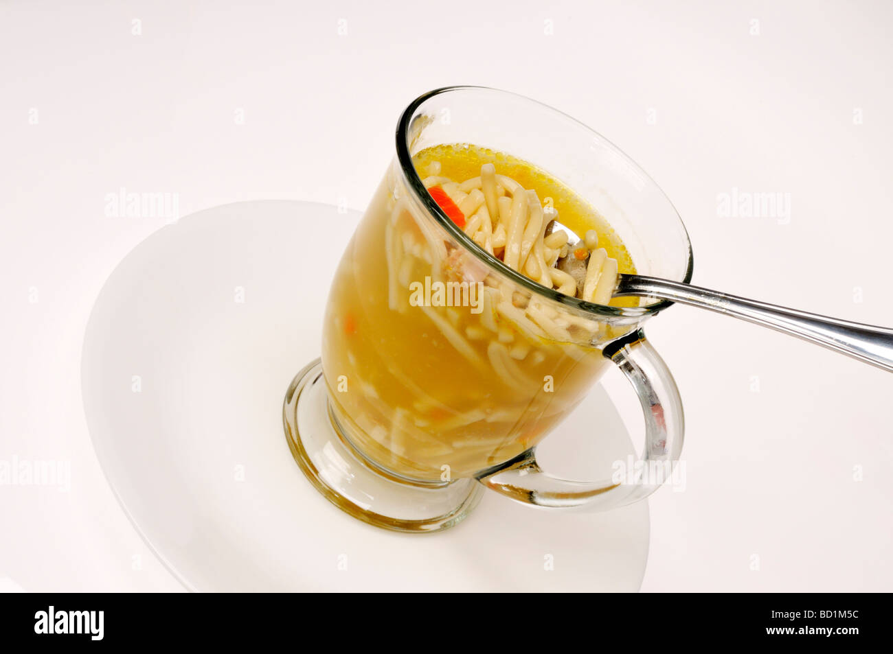 Tazza di vetro di una zuppa di noodle al pollo con cucchiaio su sfondo bianco. Foto Stock