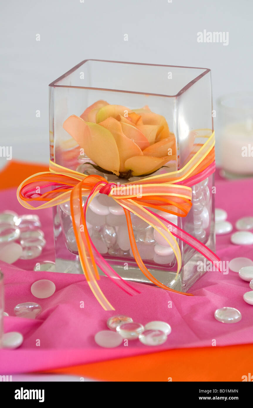 Una rosa centro tavola pezzo in un cubo trasparente con un fiocco di raso legato intorno ad esso. Foto Stock
