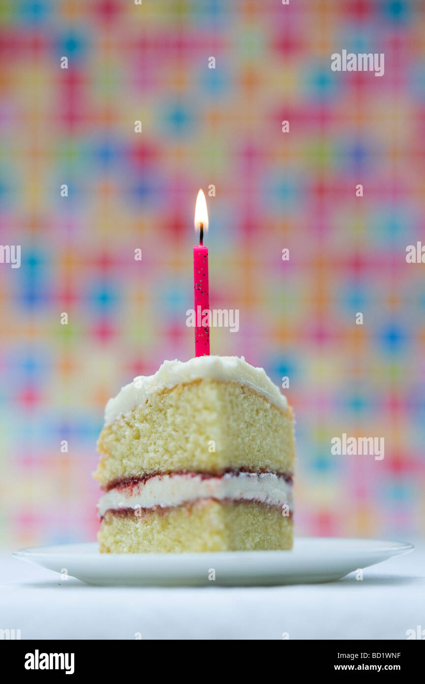 Fetta di torta di compleanno con una candela accesa contro un colorato sfondo pastello Foto Stock