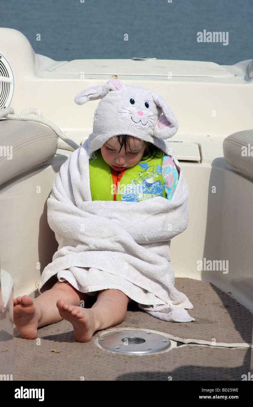Un giovane bambino seduto in una barca avvolto in un asciugamano molto stanca Foto Stock