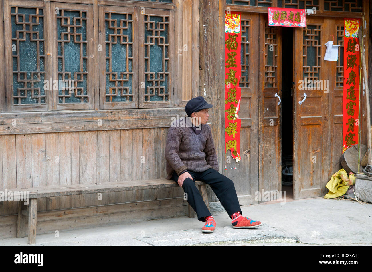 Uomo seduto fuori tipica casa in legno che caratterizza un villaggio Dong Zhaoxing Guizhou Cina Foto Stock