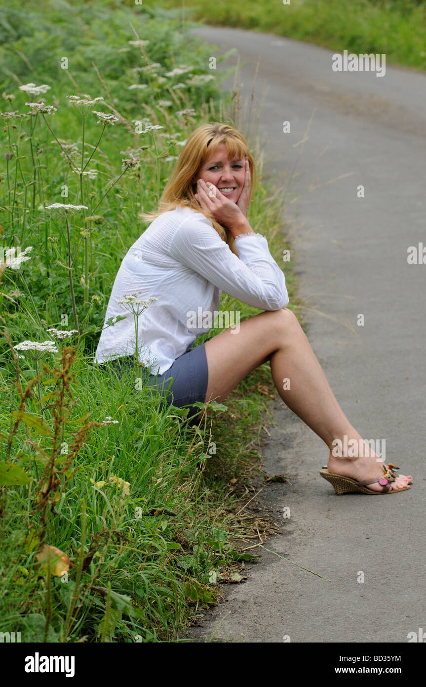 Donna matura che indossa una camicia bianca e gonna corta seduta sul ciglio  della strada Foto stock - Alamy