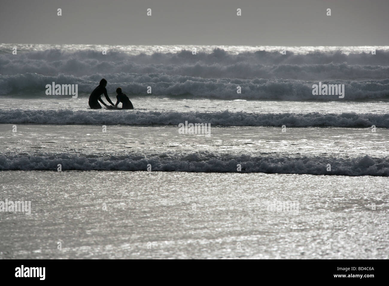 Area del Watergate Bay, Inghilterra. Stagliano vista di due surfers utilizzando la stessa tavola da surf su un mare tempestoso giorno. Foto Stock