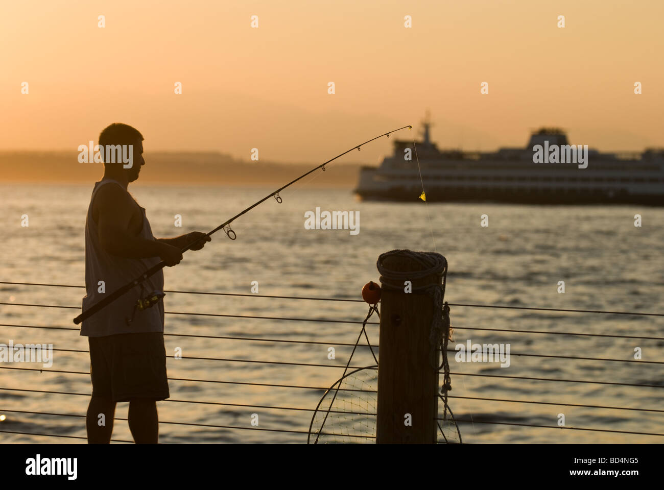Un uomo pesci off molo ad Alki Beach Park a Seattle. Foto Stock