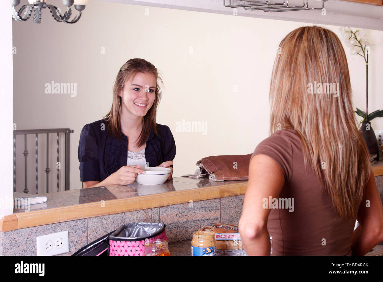 Figlia di mangiare la prima colazione mentre mamma rende il pranzo per la scuola Foto Stock