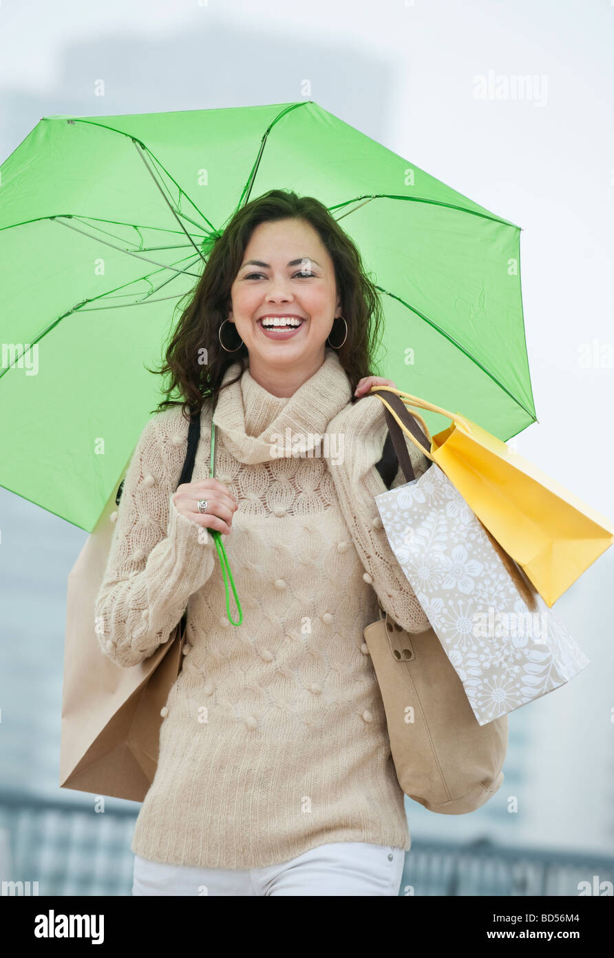 Una donna con le borse della spesa sotto la pioggia Foto Stock