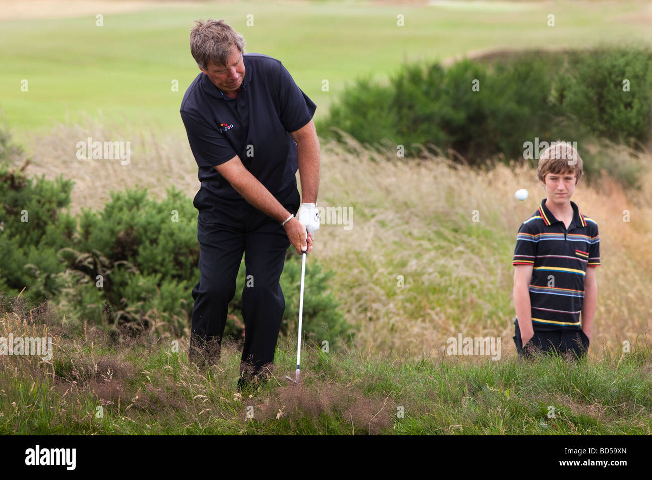 Barry Lane Professional Golfer giocando un chip sparato fuori dell'erba lunga con un piccolo ragazzo guardando a Kilmarnock Barassie GC Foto Stock