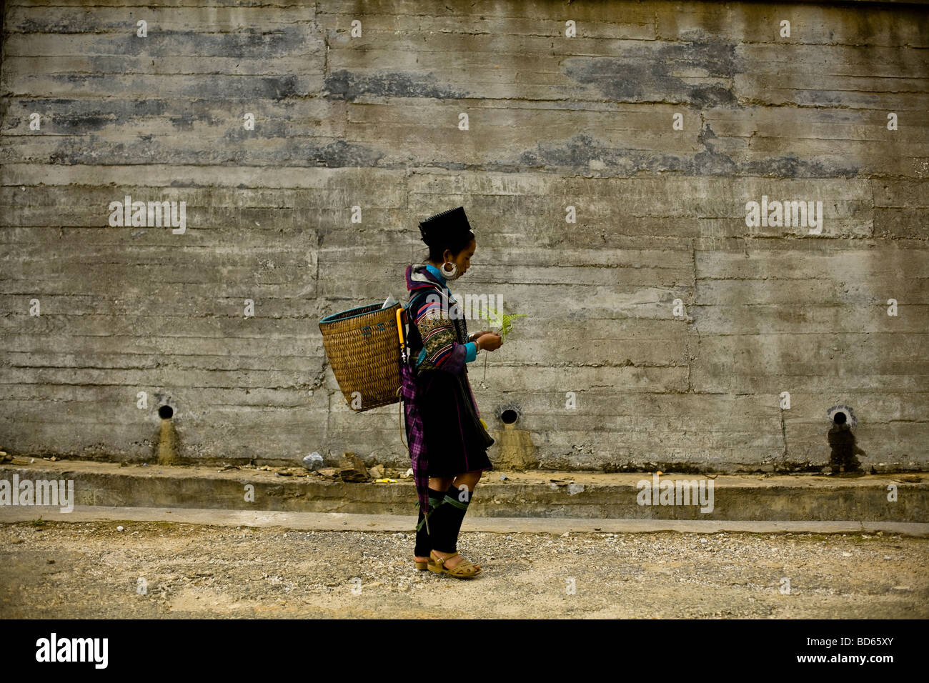 Un Nero donna Hmong passeggiate lungo passato un nuovo muro di cemento di Sapa in Vietnam del nord Foto Stock