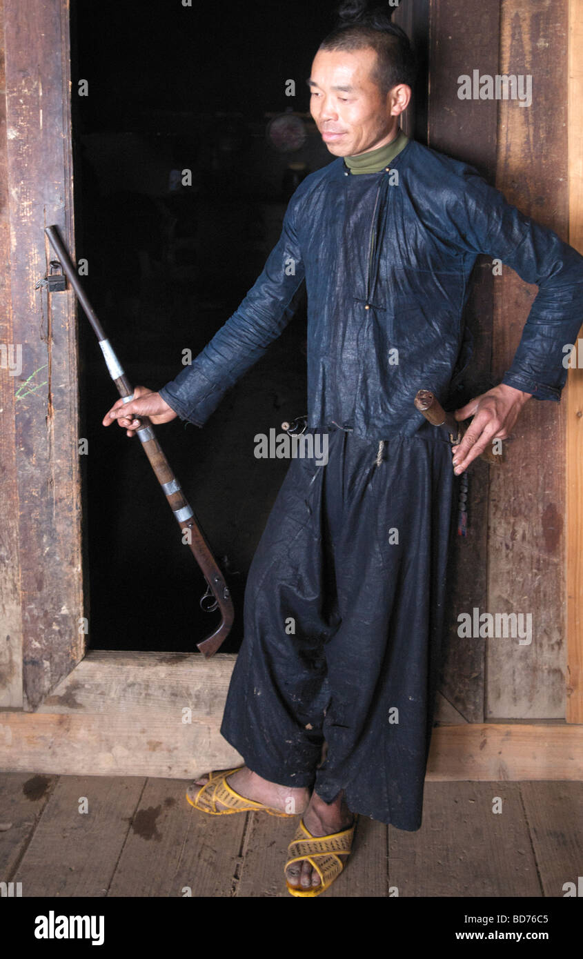 Interior Basha Miao l uomo con la pistola in piedi nella porta Congjiang County Guizhou Cina Foto Stock