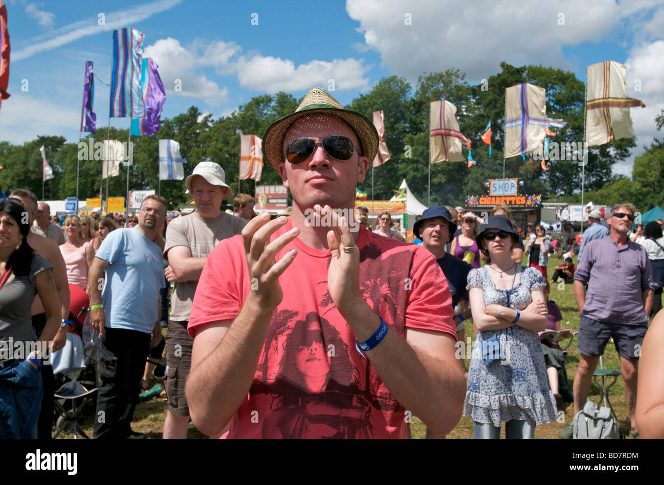 Close up ritratto di un WOMAD festival di musica di uomo con trilby e occhiali da sole battendo con un festival folla e bandiere dietro di lui Foto Stock