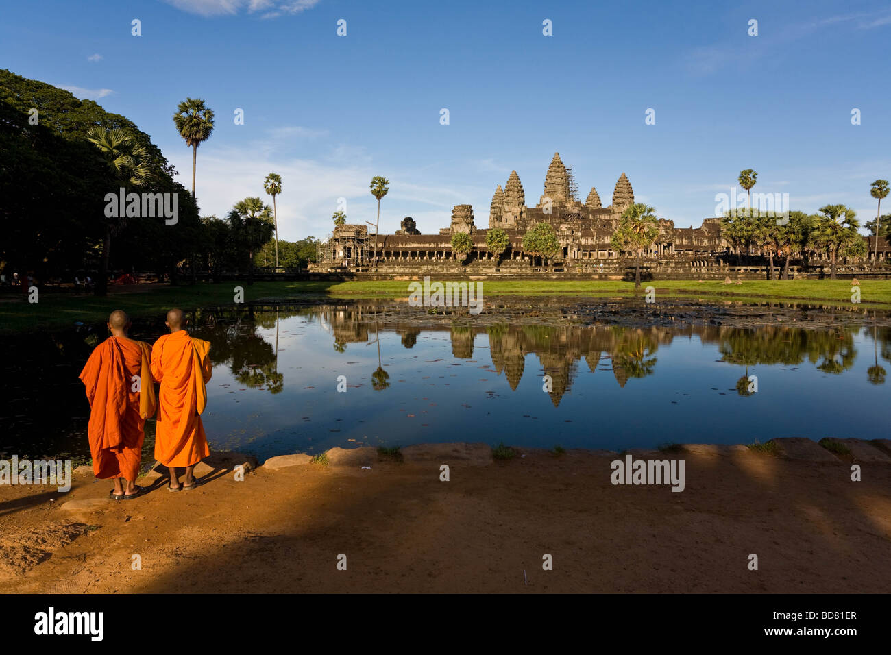 Visualizzazione classica di Angkor Wat attraverso le piscine con una chiara riflessione, con due arancio-derubato monaci in primo piano Foto Stock