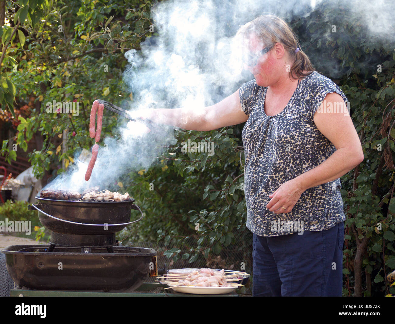 Una donna la cottura di salsicce su un Barbecue smokey Foto Stock