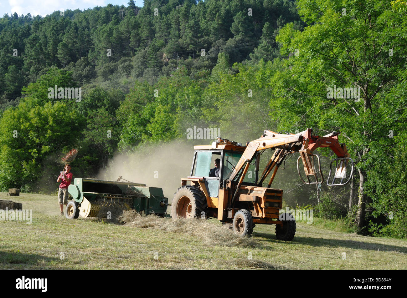 Un trattore balle di fieno in un campo nelle zone rurali della Francia. Dopo diverse settimane di tempo secco il processo realizzato un enorme quantità di polvere. Foto Stock