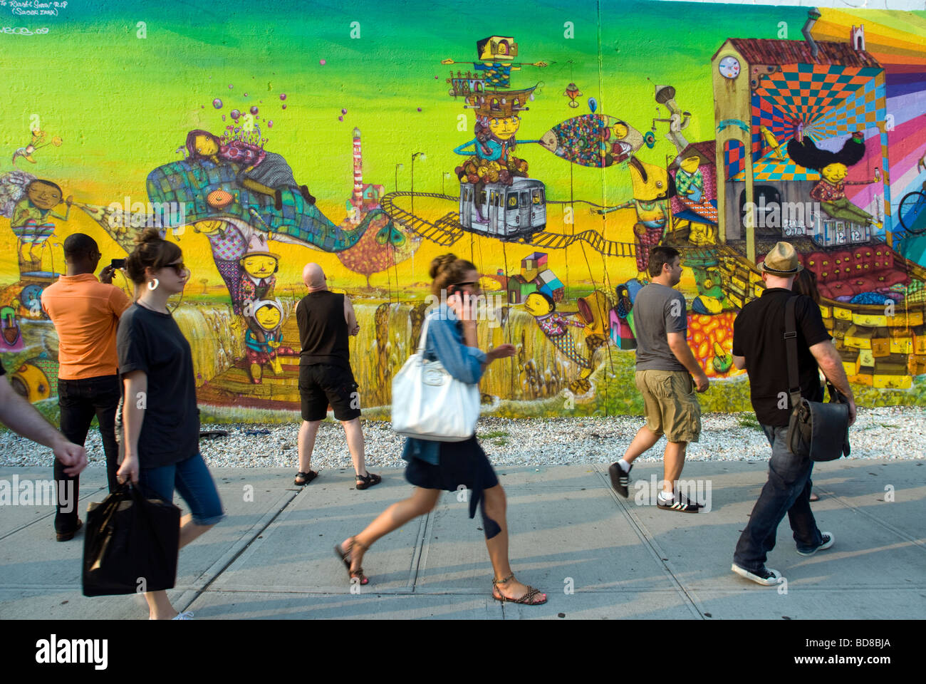 Passerby rispettare o ignorare un murale dal brasiliano artisti di graffiti Os Gémeos in New York Foto Stock