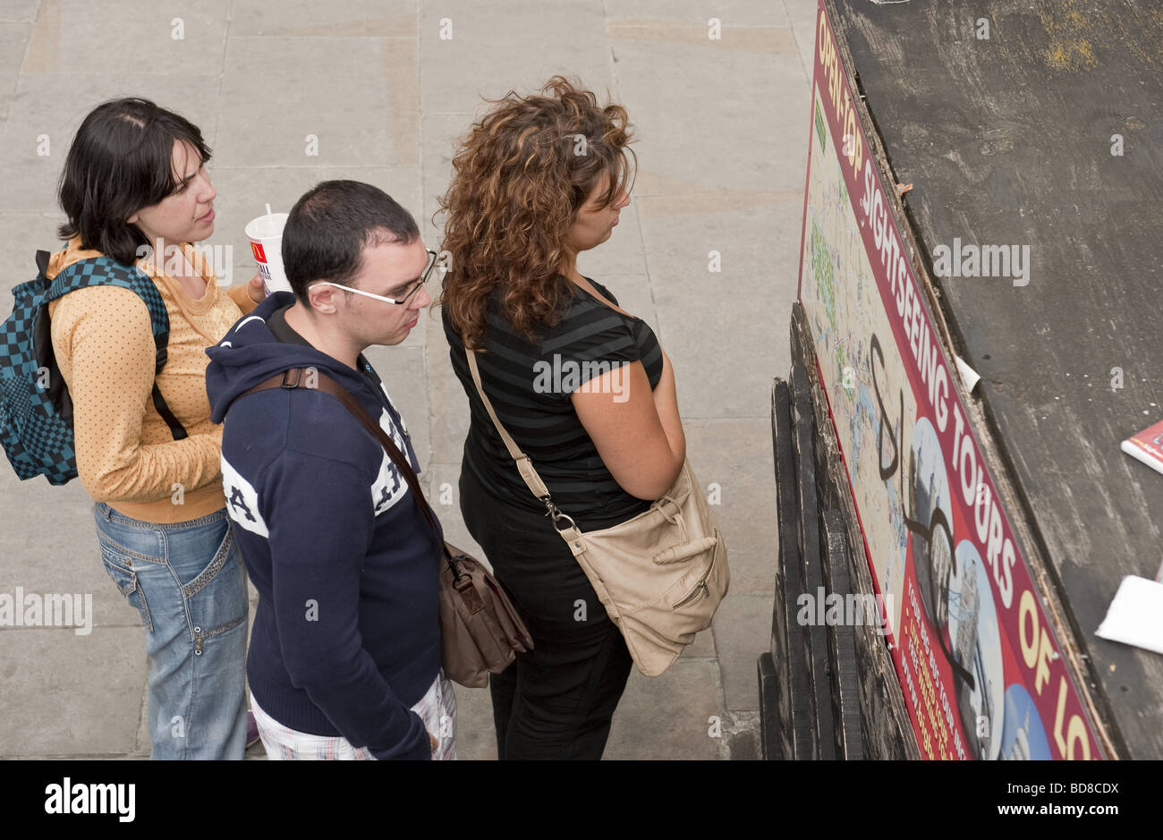 Un elevato angolo di visualizzazione di un gruppo di turisti in cerca di una parete montata London Bus Tour mappa completa con grafitti Foto Stock