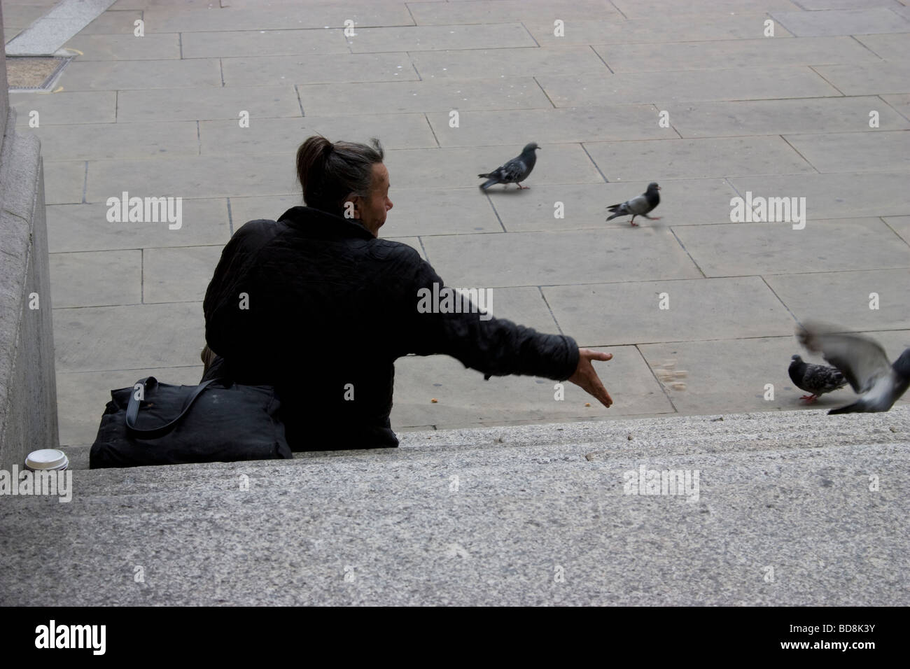 Anziana donna senzatetto alimentazione di uccelli piccioni il pane su fasi di royal exchange LONDON REGNO UNITO Foto Stock