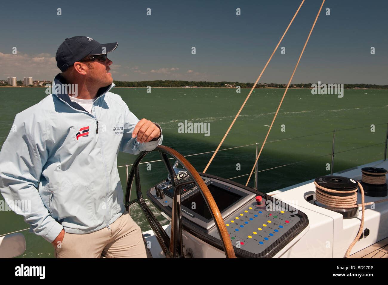 Capitano sulla ruota di yacht a vela Liara come lei le vele verso il basso Southampton acqua per il Solent Foto Stock