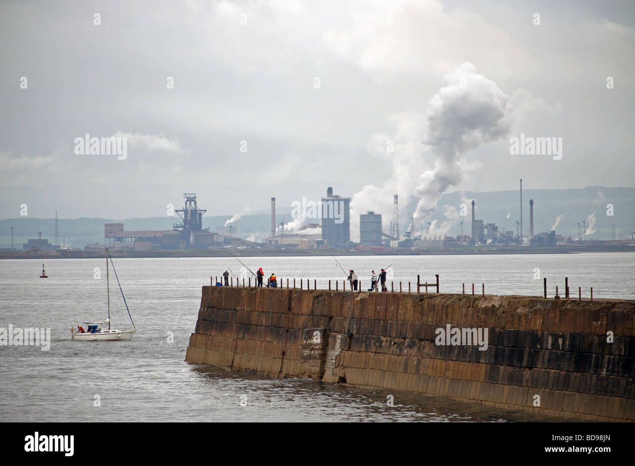 I pescatori pesca dal promontorio in Hartlepool con la Corus fabbrica di acciaio a Redcar in background Foto Stock