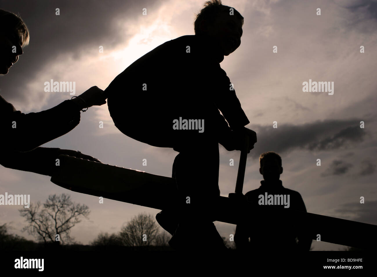 Silhoutte di un ragazzo e 2 adulti in un parco giochi Foto Stock