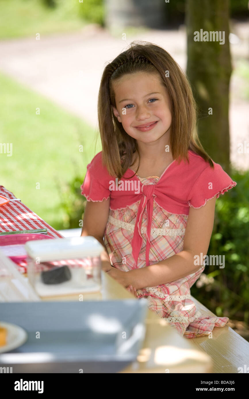 Carino 7 anno vecchio ragazza seduta all'aperto presso il picknick table Foto Stock