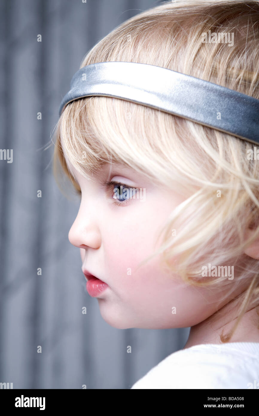 Un close up ritratto di una bambina con luminosi occhi blu. Lei ha i capelli  biondi e indossa un cerchietto per capelli in argento e una camicia bianca  Foto stock - Alamy