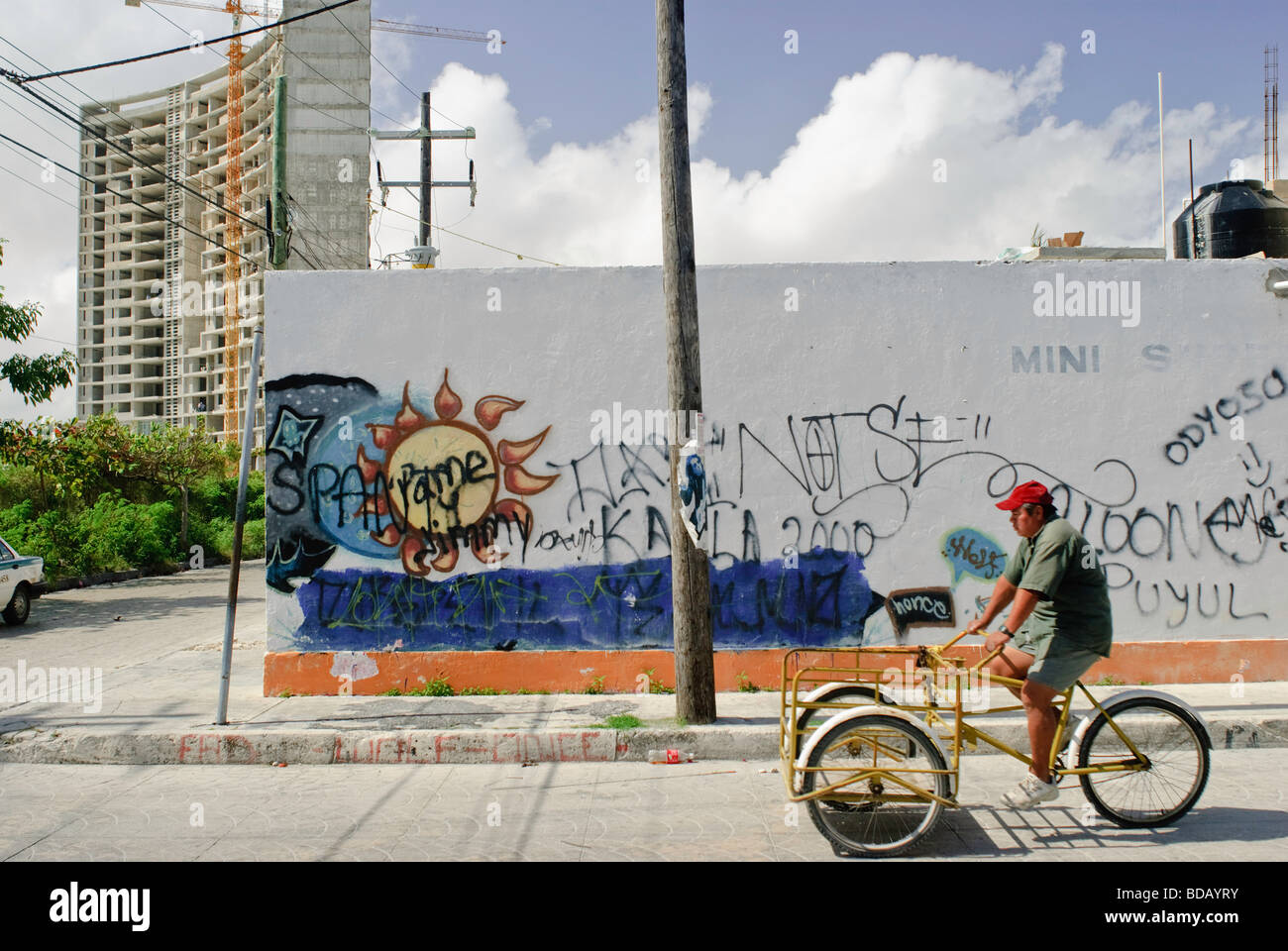 Nuovo hotel e appartamento costruzione sorge al di sopra di un angolo di strada e un uomo su un triciclo in una classe bassa quartiere di Cancún Foto Stock