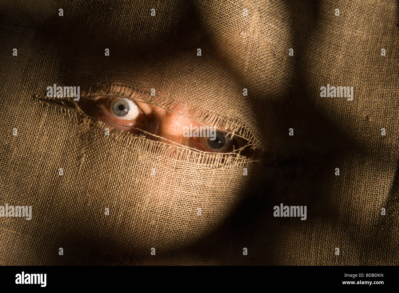 Minaccioso occhi guardano attraverso una fessura strappato il panno. Foto Stock