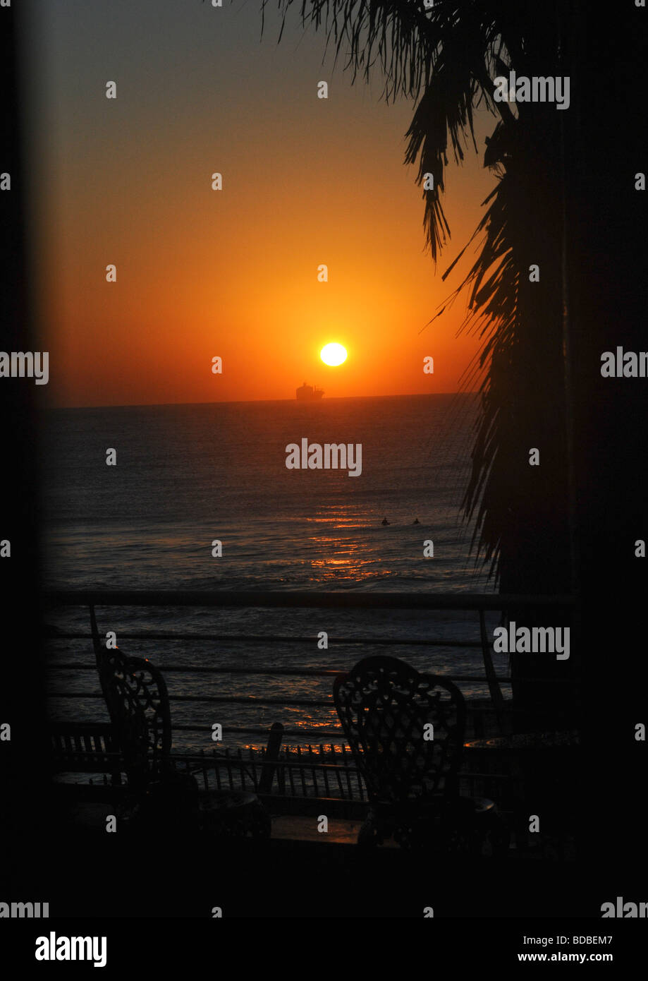 Mattina presto all'alba sopra l'orizzonte oltre il mare con la silhouette di una nave, la gente di nuoto, veranda, e una parte di un albero di palma. Foto Stock