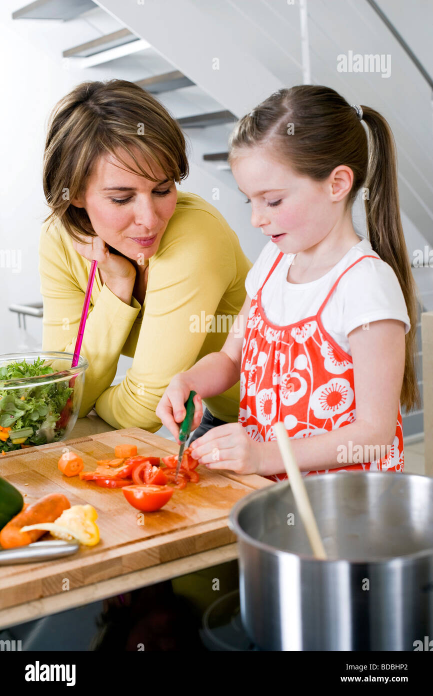 Madre guarda la sua figlia di tagliare le verdure Foto Stock