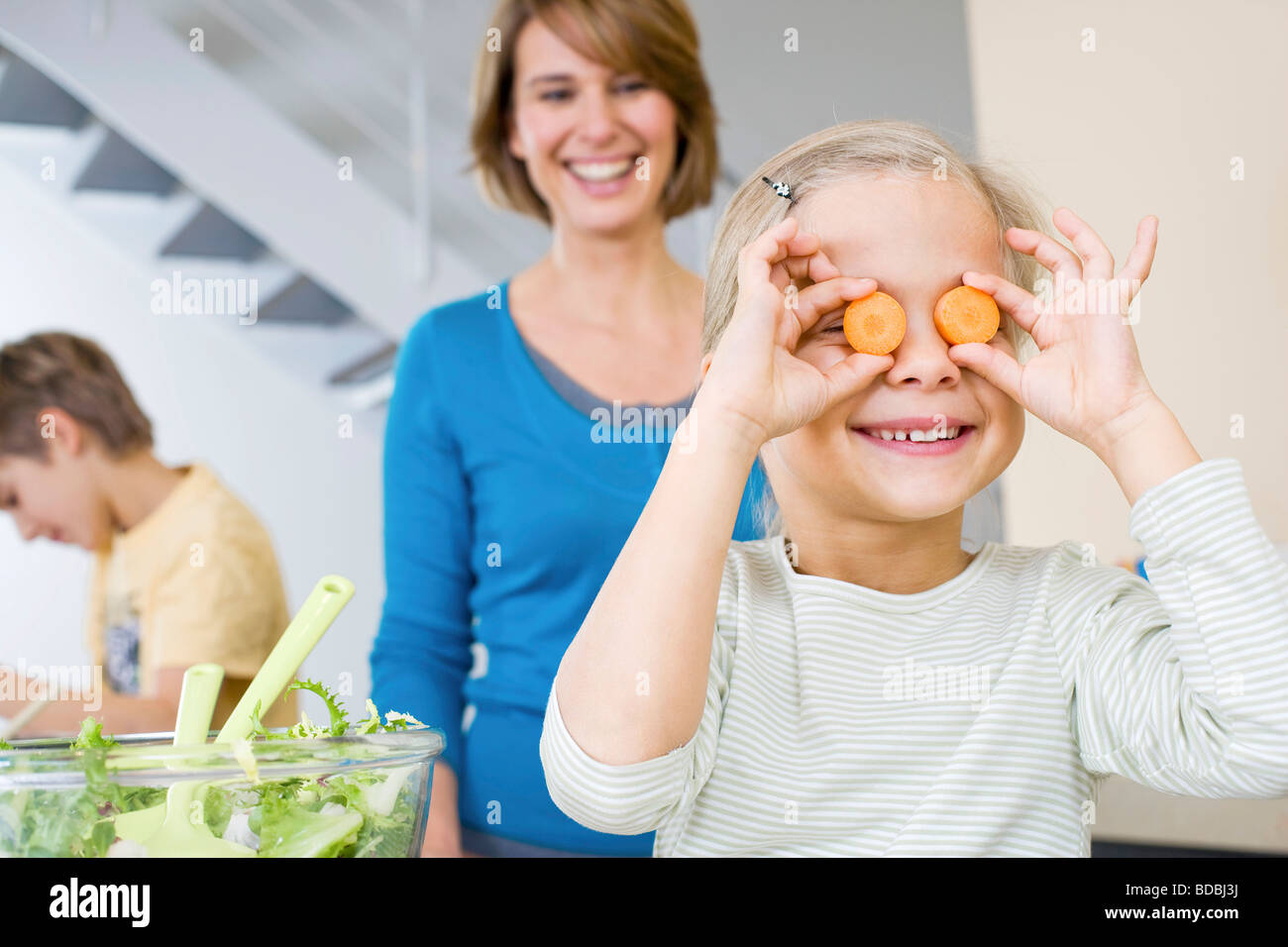 Madre guarda la figlia giocare con fette di carota in cucina Foto Stock