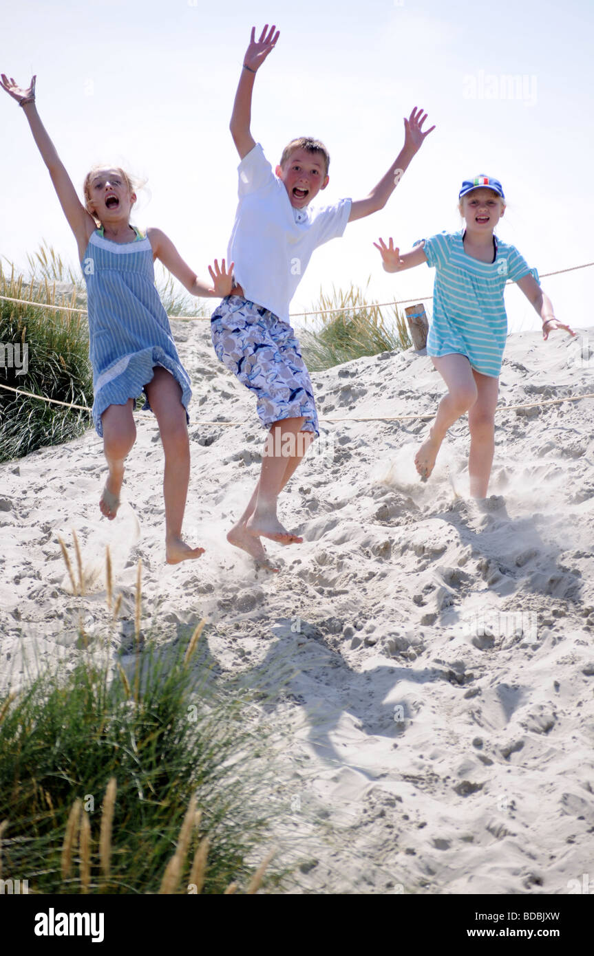 Royalty free fotografia di un ragazzo e una ragazza salta fuori da dune di sabbia sulla spiaggia in estate sulla costa inglese UK Foto Stock