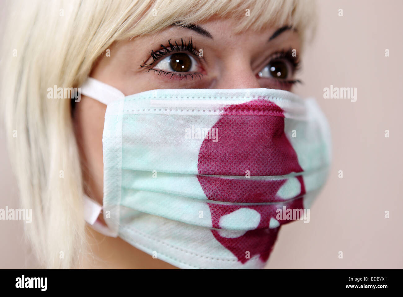 Una ragazza bionda indossa un chirurgiche personalizzate la maschera per il viso con un cranio rosso stampato. Foto Stock