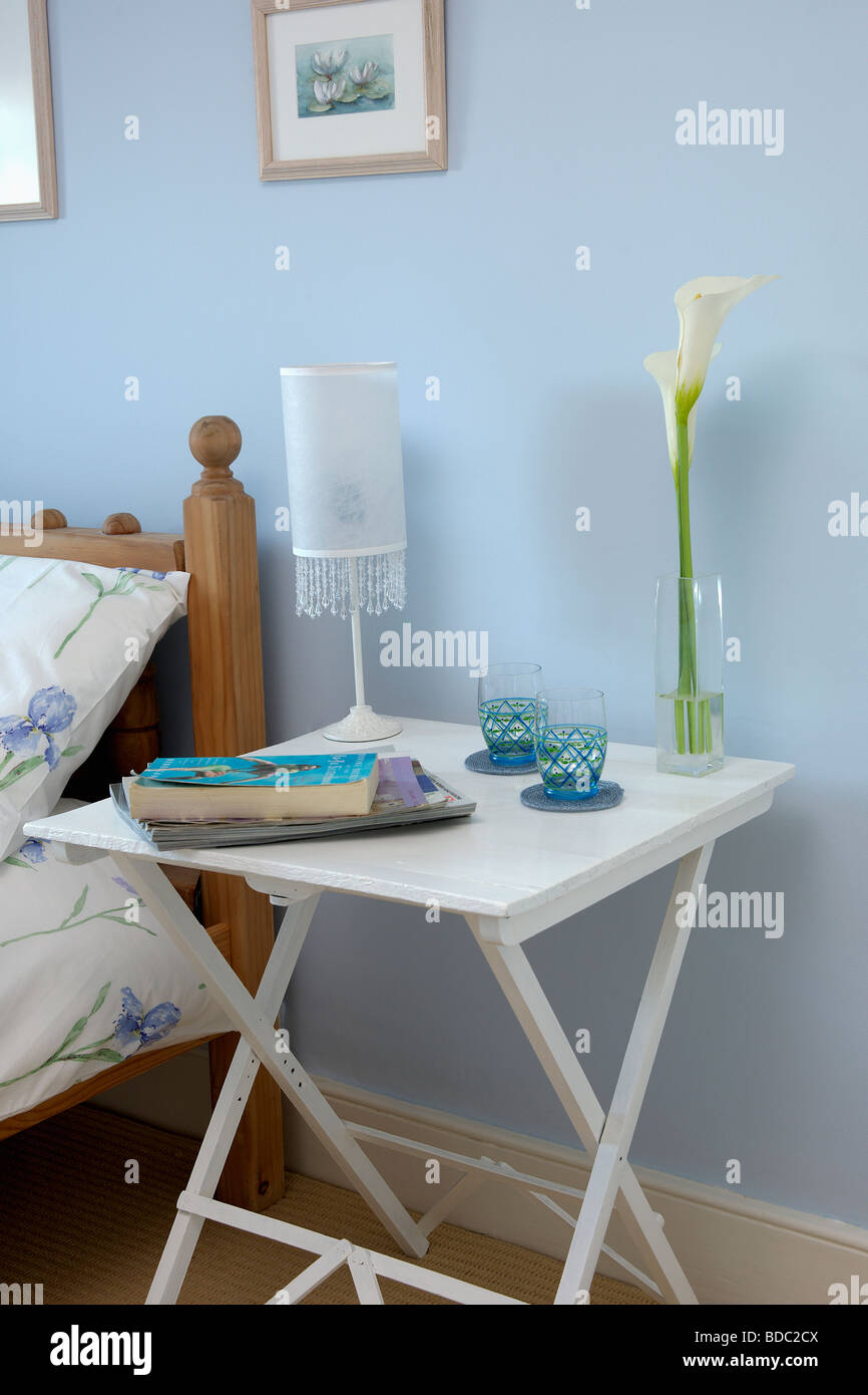Libri e la lampada bianca sul piccolo dipinto di bianco comodino in pastello blu camera da letto Foto Stock
