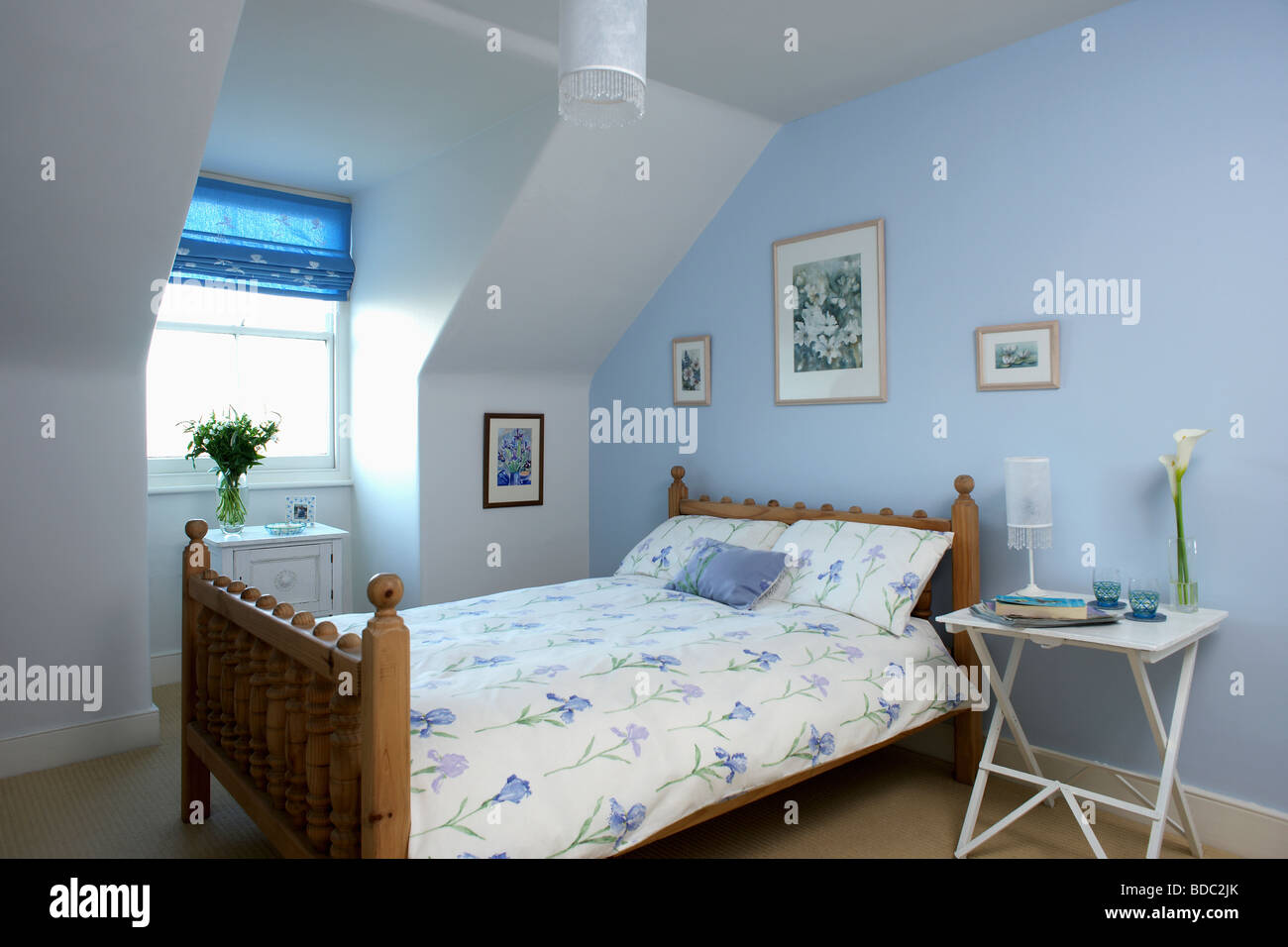 Iris blu quilt modellato e cuscino sul letto in legno in pastello blu mansarda camera da letto con il bianco comodino Foto Stock
