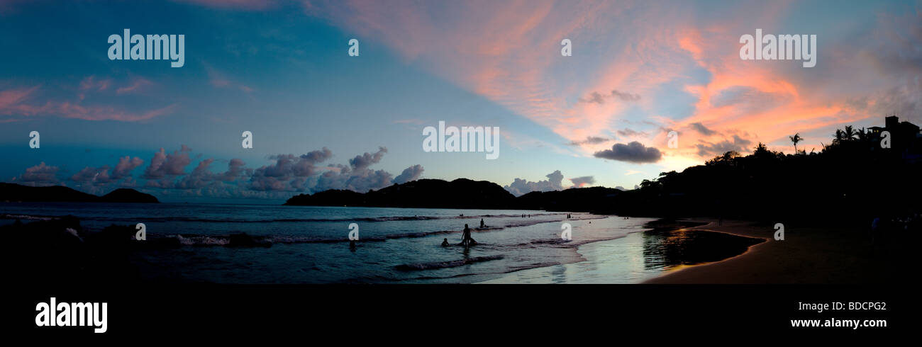 Riprese panoramiche del tramonto sulla spiaggia di Playa La Ropa a Zihuatanejo, Messico, con sagome di persone a giocare tra le onde Foto Stock