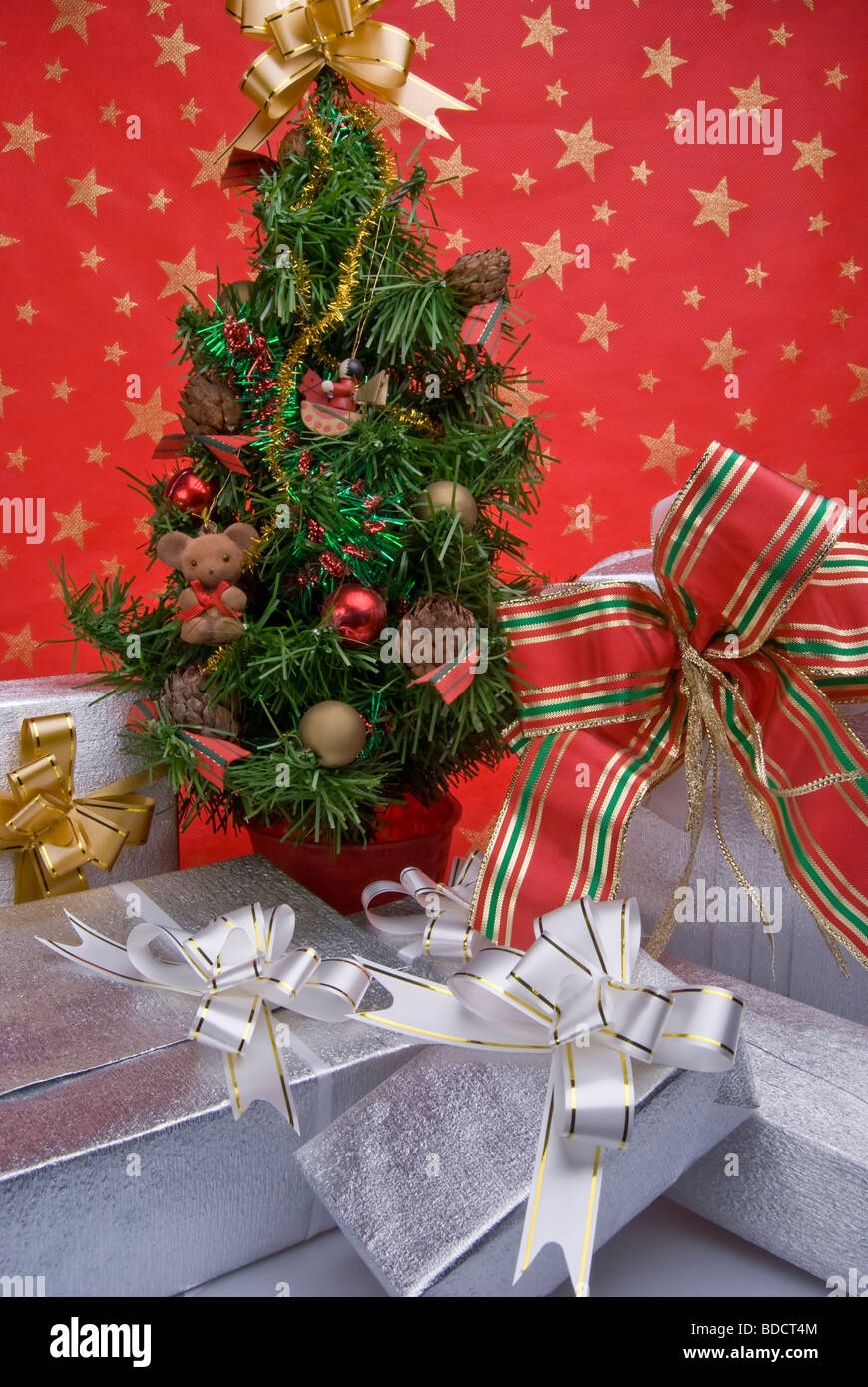 Cinque pacchetti regalo sotto un piccolo albero di Natale su uno sfondo di colore rosso decorato con stelle dorate Foto Stock
